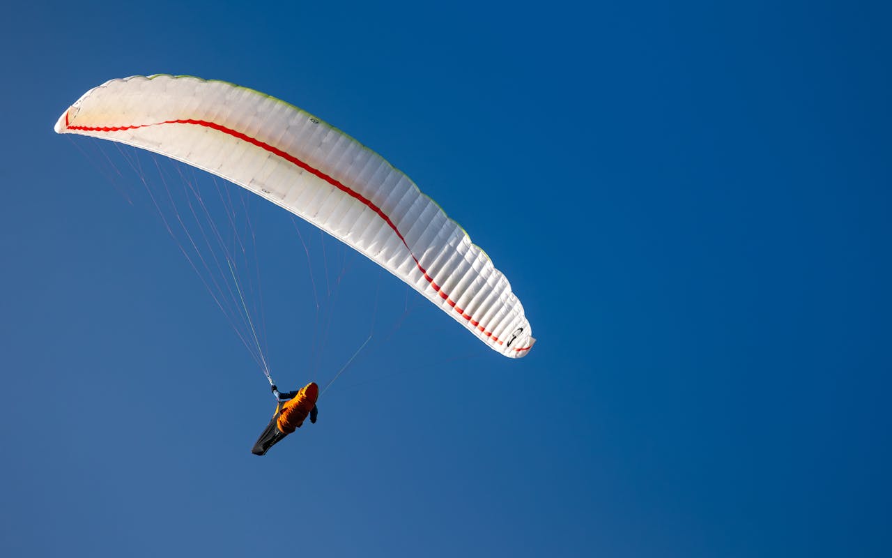 A lone paraglider enjoys the thrill of flight against a clear blue sky, capturing a moment of adventure.
