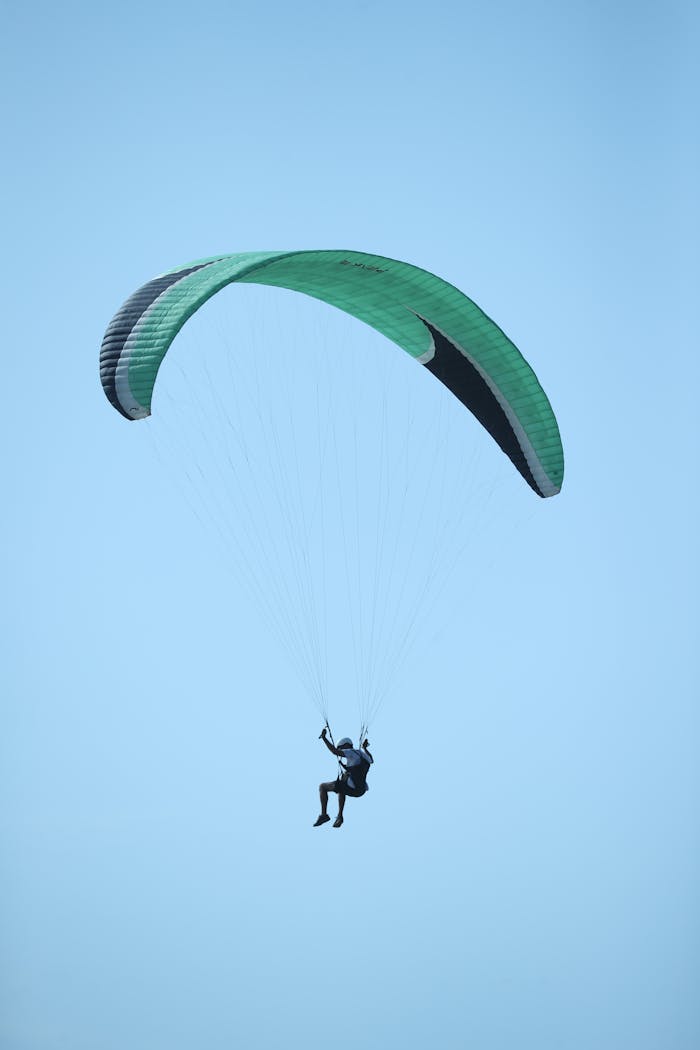 Experience the exhilaration of paragliding with vibrant green and black wings against a clear sky.