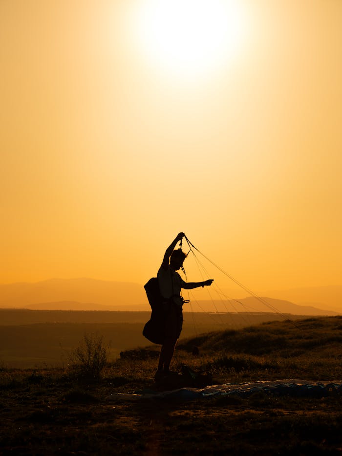 A paraglider silhouetted against a vibrant yellow sunset sky in a rural landscape.