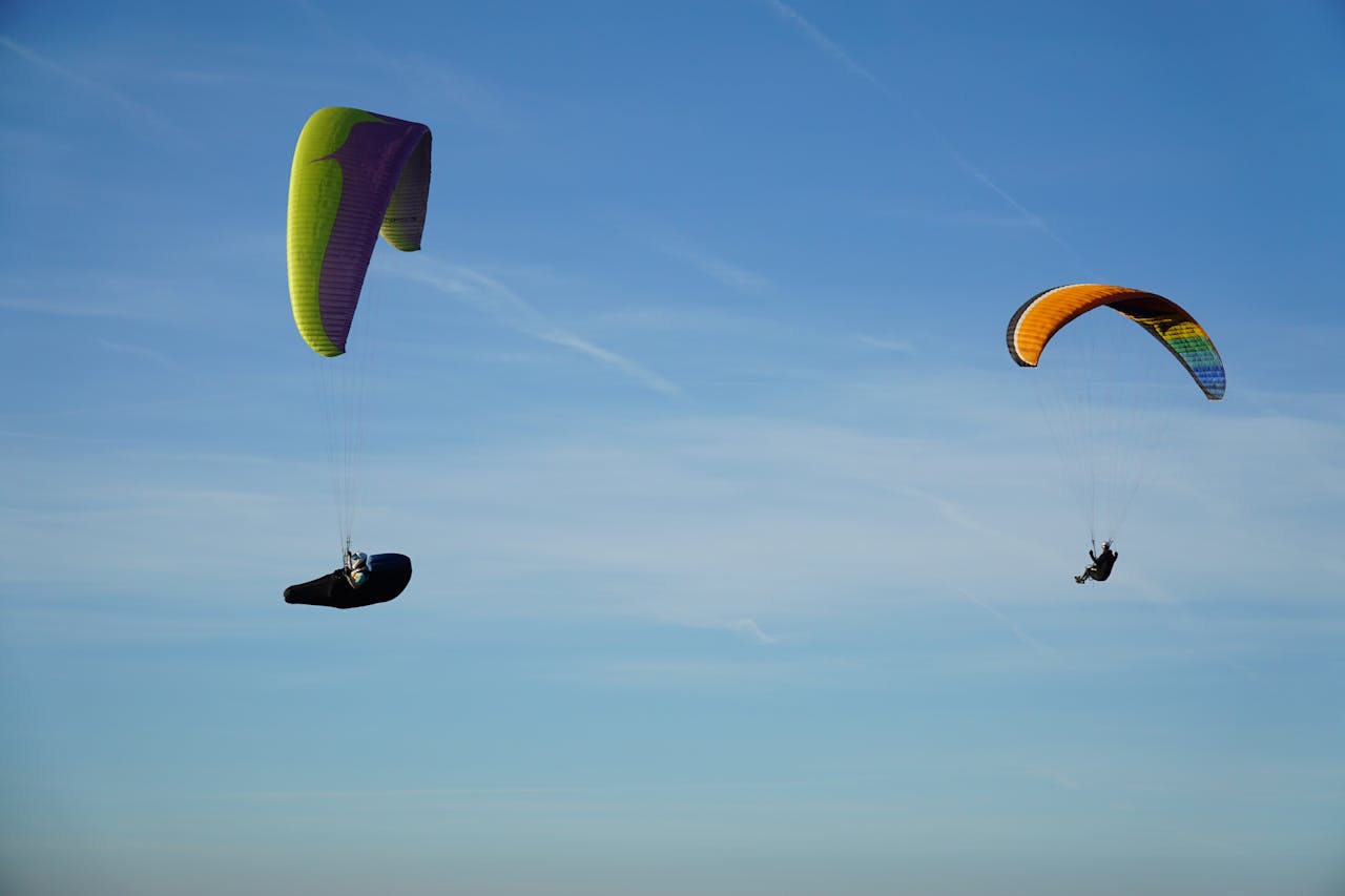 Two colorful paragliders soar gracefully against a clear blue sky in Millau, France.
