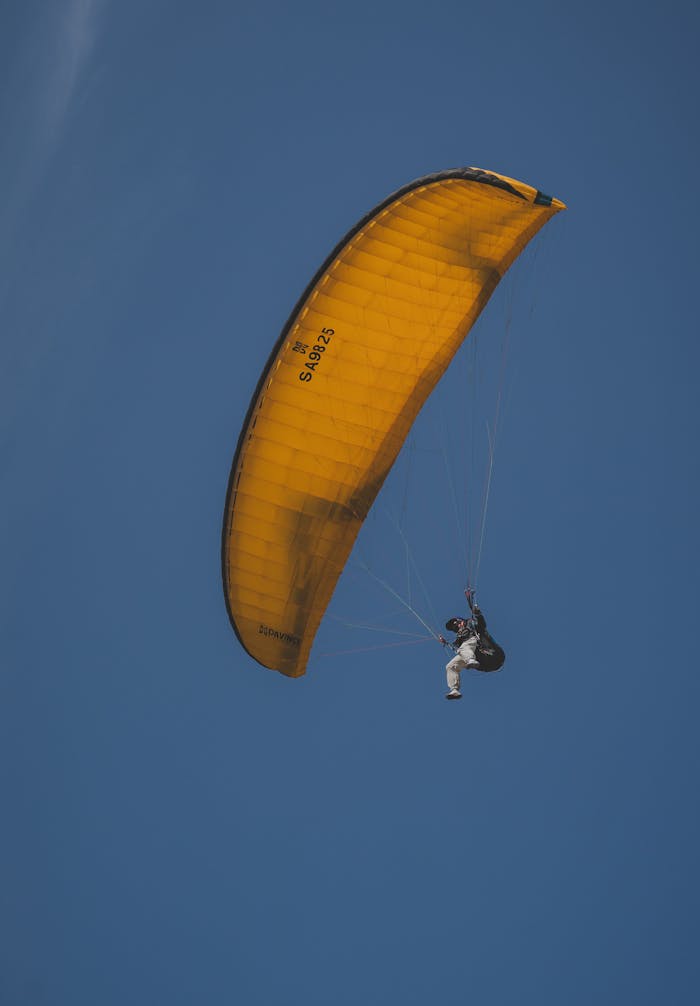 A paraglider with a yellow canopy soaring high in a clear blue sky, capturing the essence of adventure.