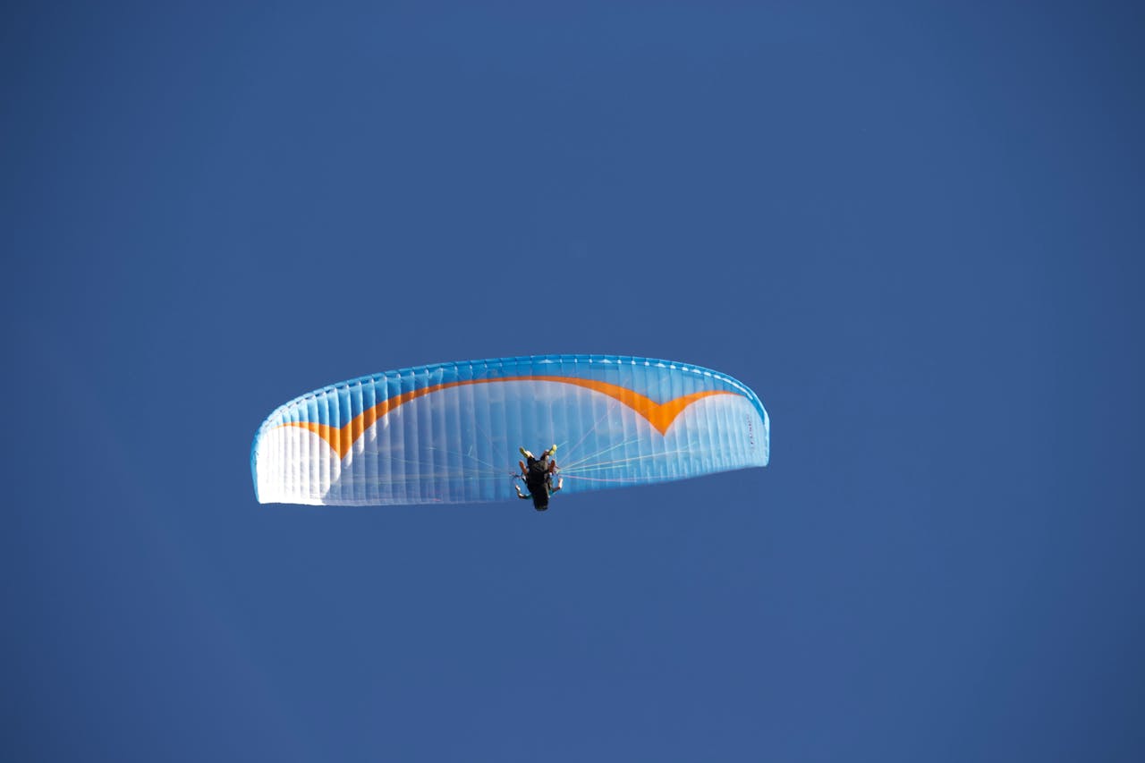 Mastering the First Impression: Your intriguing post title goes here From below of anonymous paraglider with blue parachute flying against blue cloudless sky in nature in sunlight during practicing outside