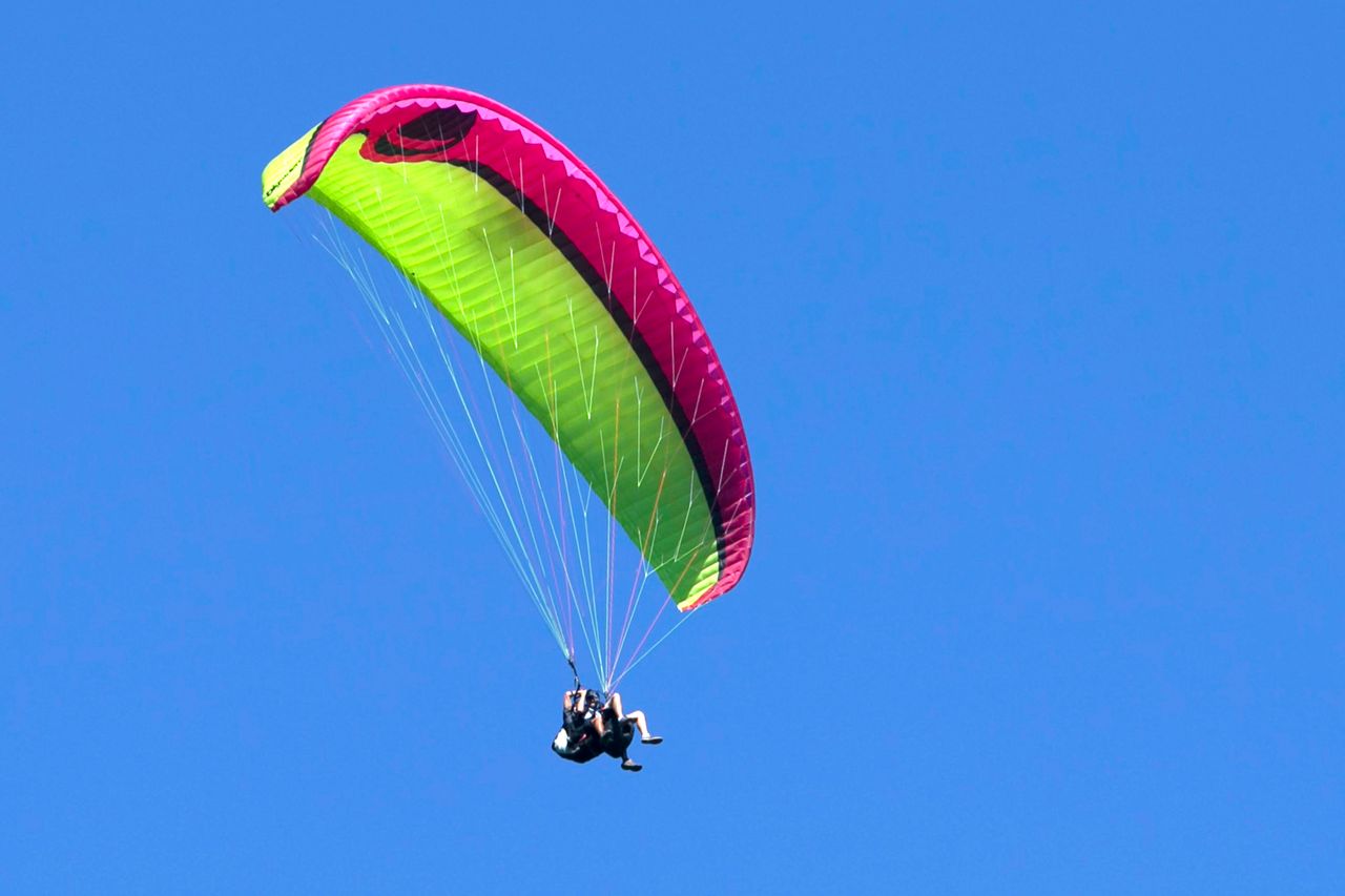 Brightly colored paraglider in flight against a clear blue sky, capturing the thrill of adventure.