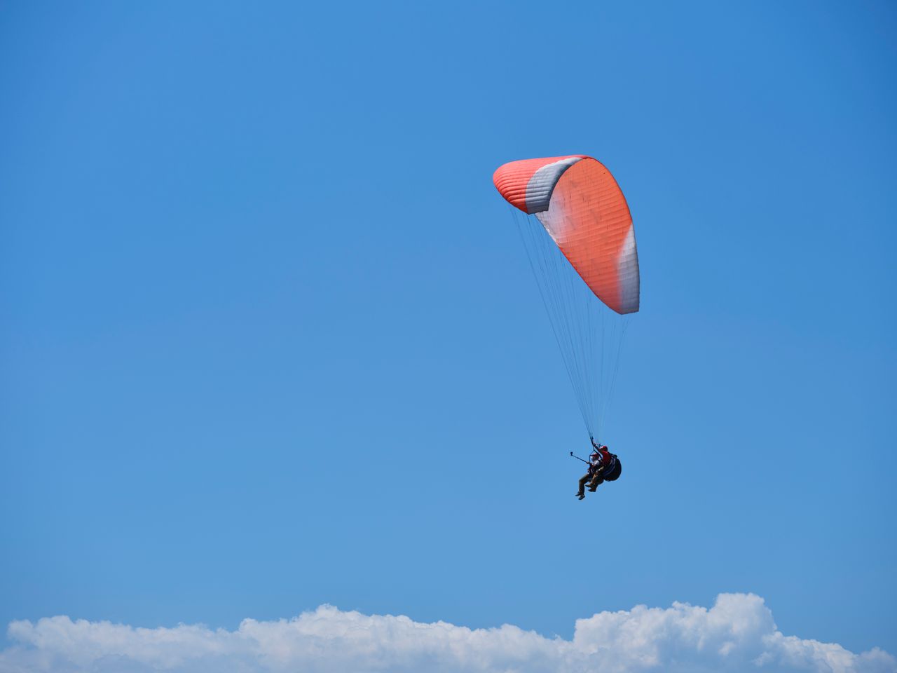 gallery-02 Paraglider soaring gracefully with a vibrant red parachute against a blue sky backdrop.