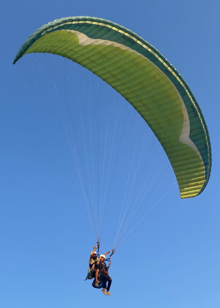 services-02 Two people enjoy paragliding against a clear blue sky, embracing adventure.