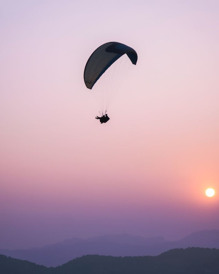 services-01 Silhouette of a paraglider soaring against a vibrant sunset over mountains. Adventure and tranquility in harmony.