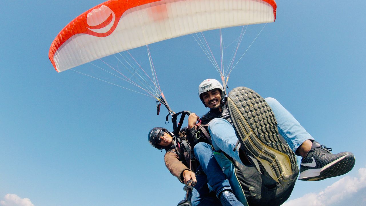 gallery-05 Two men enjoying tandem paragliding against the clear blue sky.